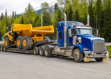 Blue flatbed truck hauling heavy construction equipment