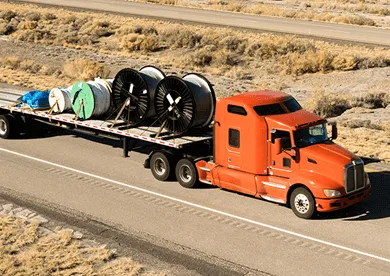 Orange semi truck hauling industrial equipment on flatbed