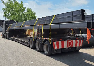 Flatbed truck transporting long steel beams with safety straps