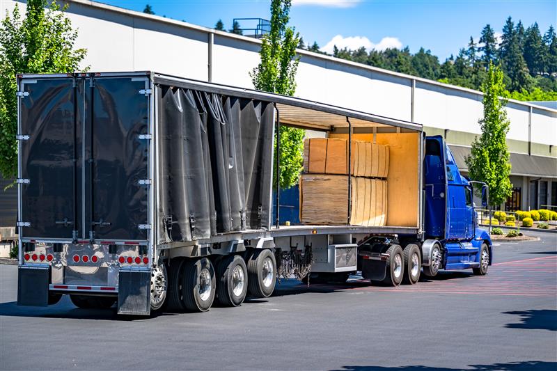 Blue semi truck with curtain-side trailer at warehouse loading dock